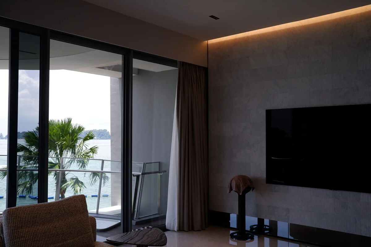 Living room with full-height curtains, warm cove lighting and a balcony